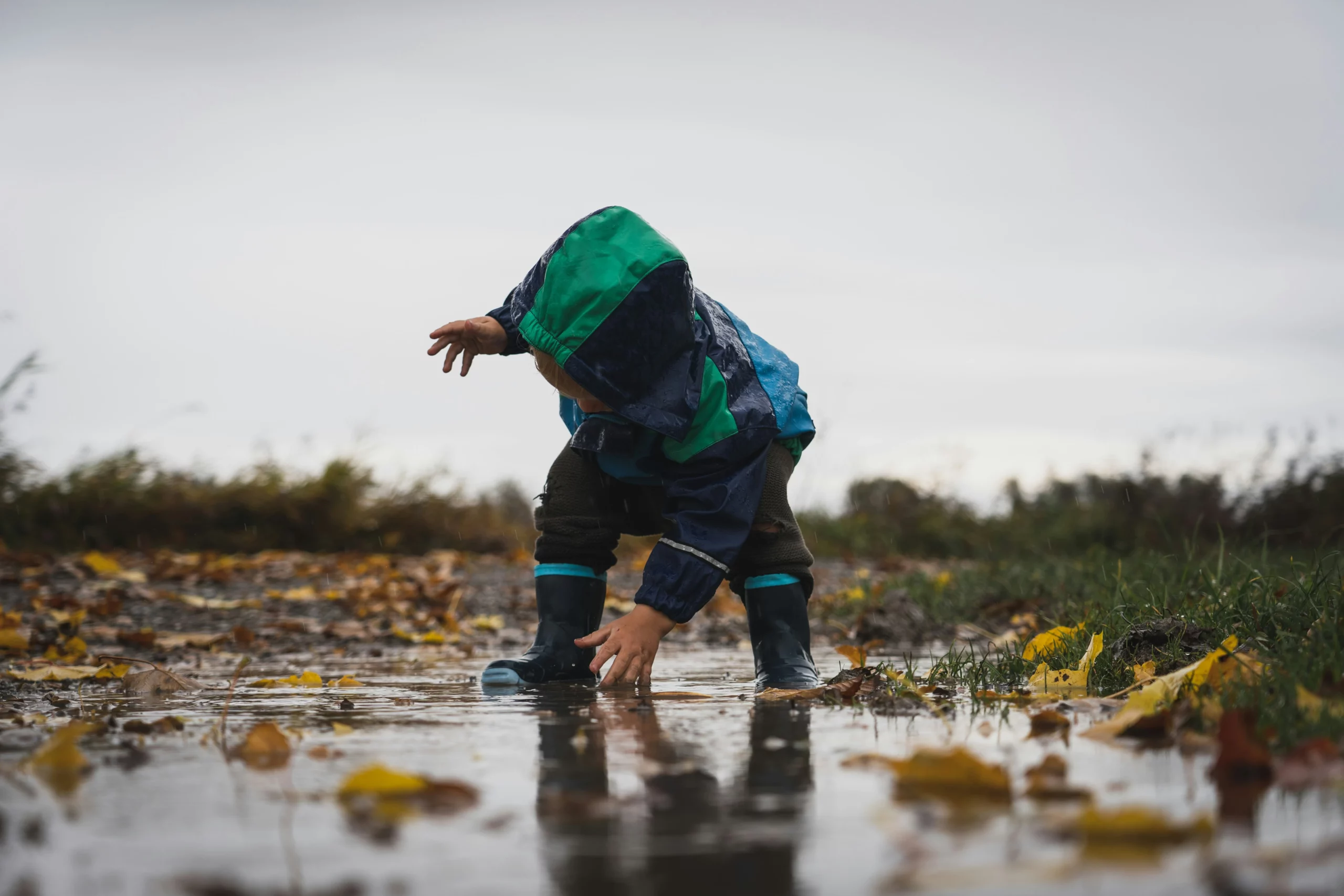 bambino con mantella e stivali di gomma per bambini in una pozzanghera