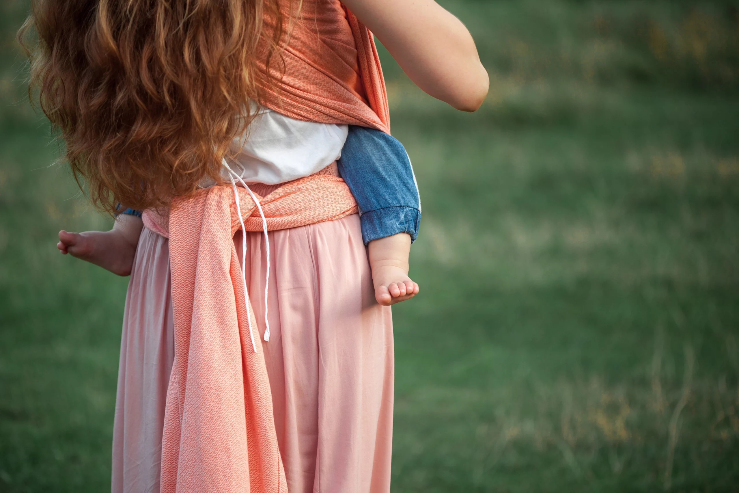 mamma vista da dietro con bambino in fascia babywearing e sfondo di campo di grano verde