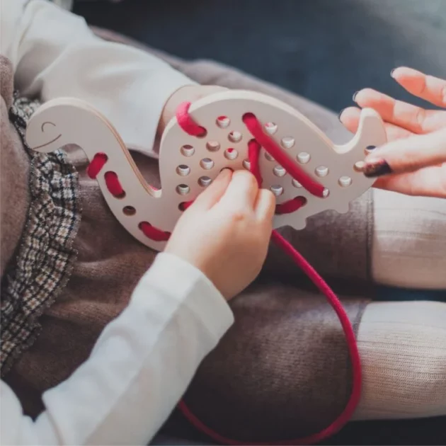 mani di bambina che gioca con Giocattolo educativo Montessori ad intreccio in legno a forma di brontosauro con lacci rossi