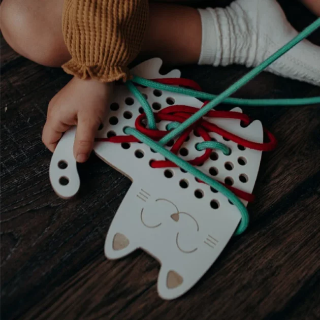 mani di bambino che gioca con giocattolo educativo Montessori ad intreccio in legno a forma di gatto con lacci verdi e rossi