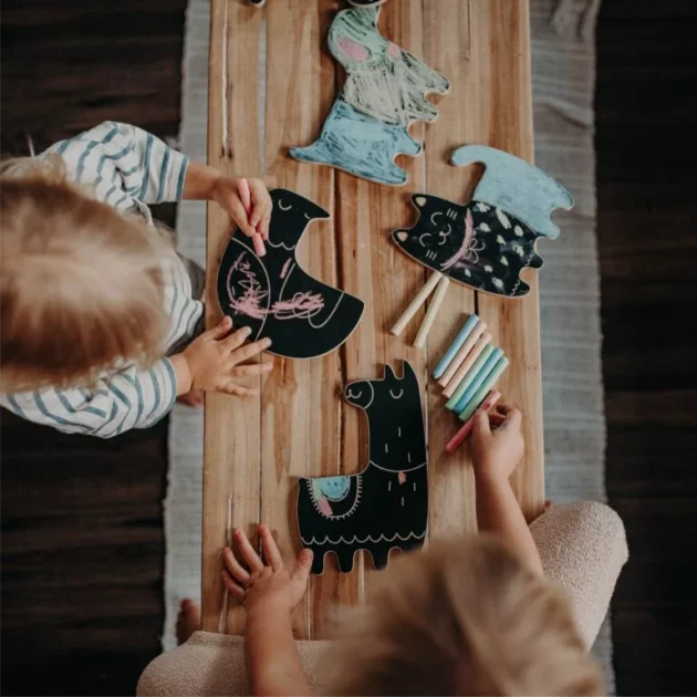 bambini che giocano su tavolo in legno con lavagne a forma di animali e gessetti colorati