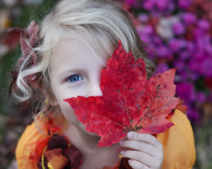 bambina con in mano una foglia di colori autunnali